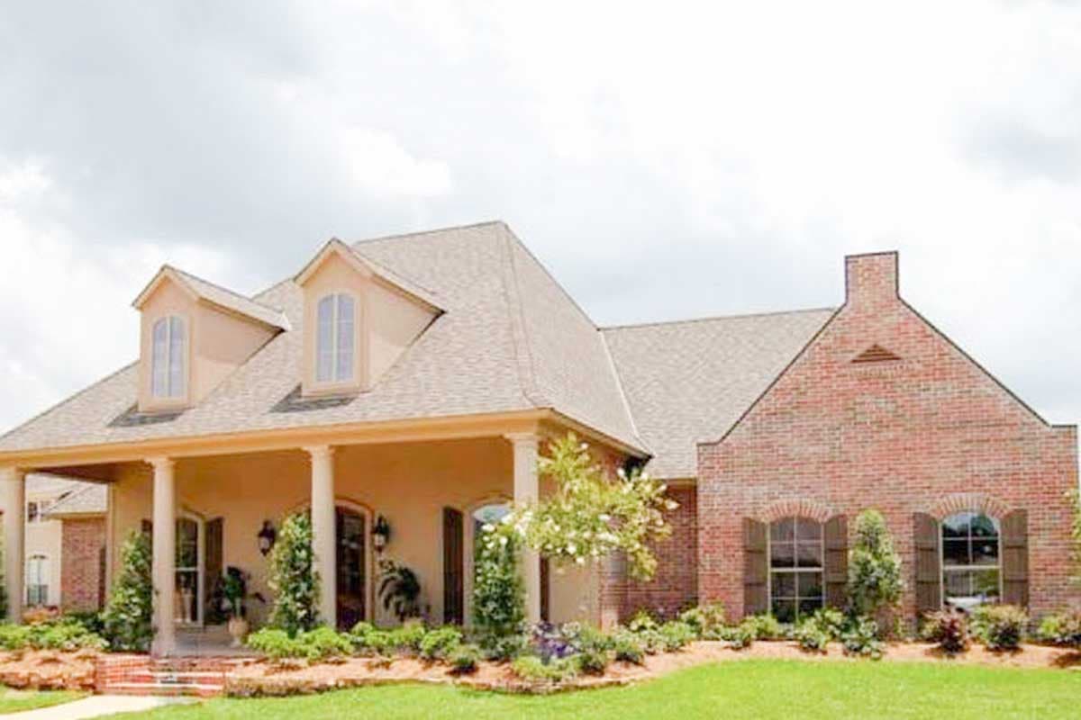 House plan exterior with covered porch, Tuscan columns, dormer windows, and brick facade with arched windows.