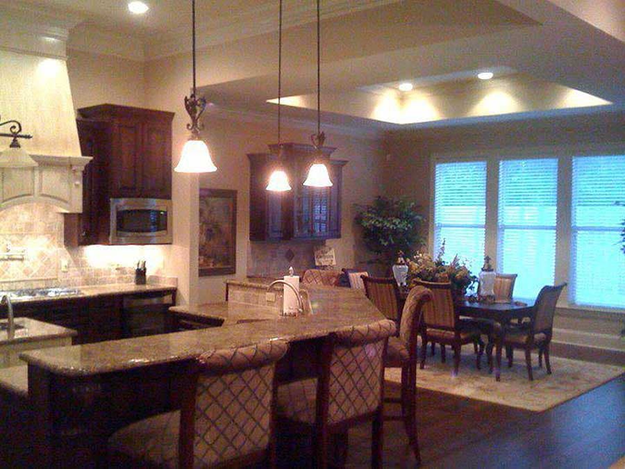 Kitchen and dining area with granite countertops, island seating, dark wood cabinetry, and a tray ceiling.