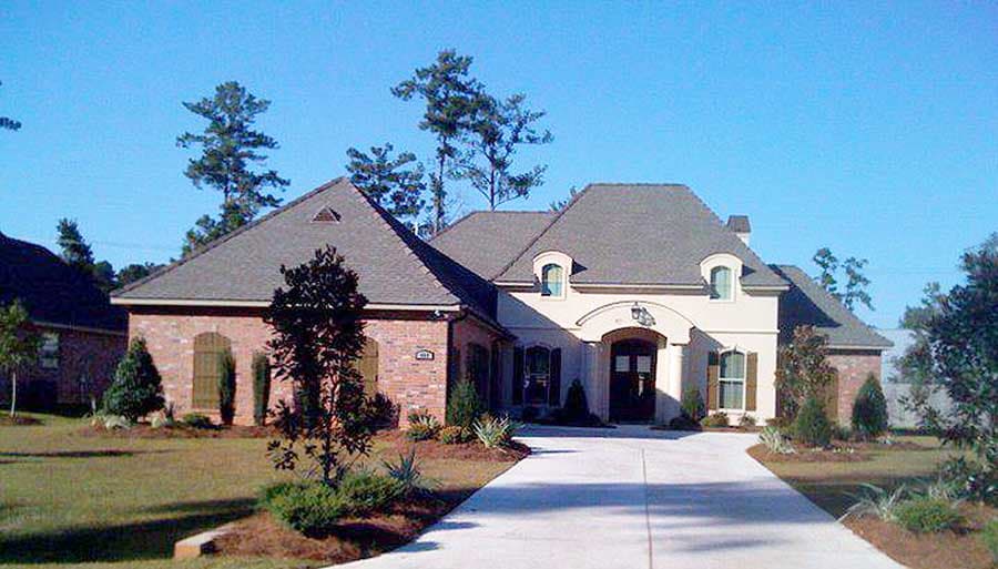House plan exterior: One-story home with brick accents, arched entryway, dormers, and varied rooflines.