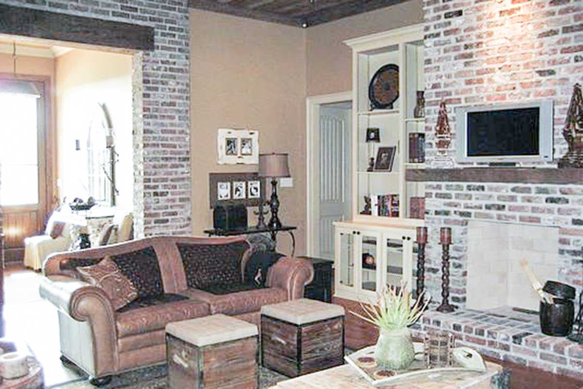 Living room with brick fireplace, built-in shelving, leather sofa, and wood beam ceiling.