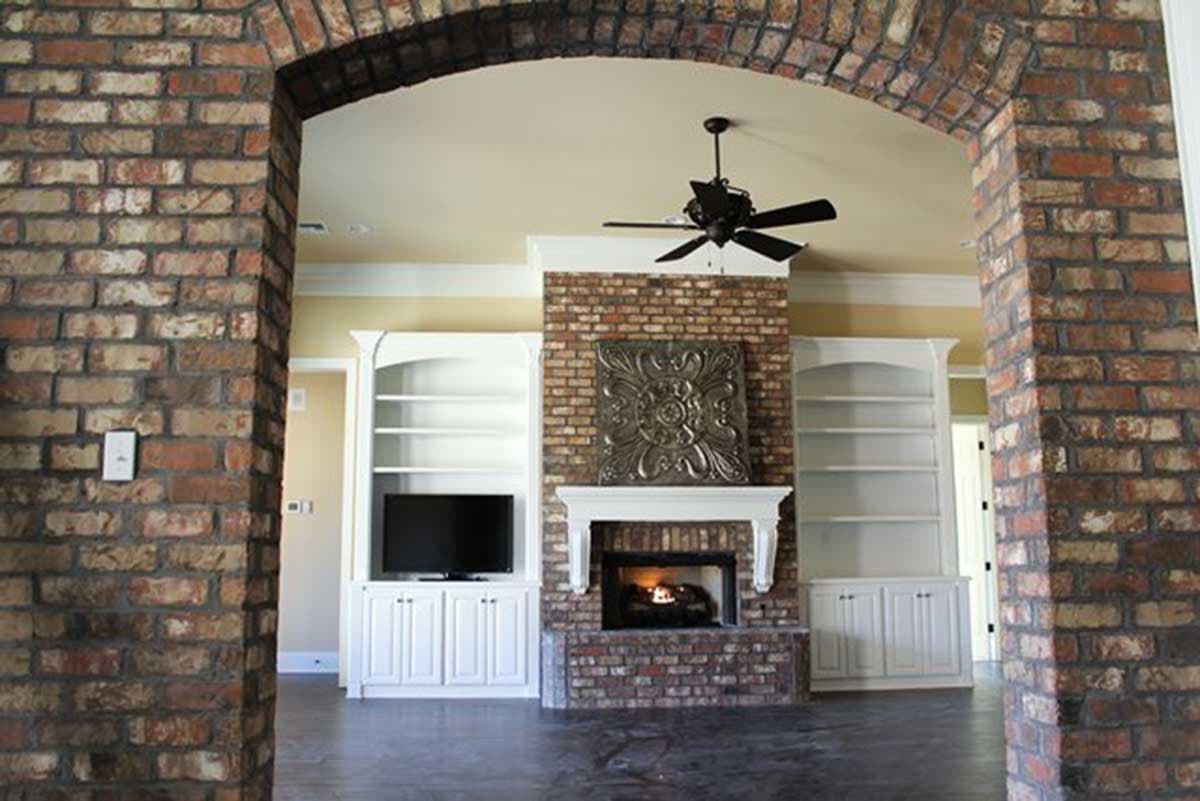 Interior view of a living area with brick fireplace, built-in shelving, and a ceiling fan.