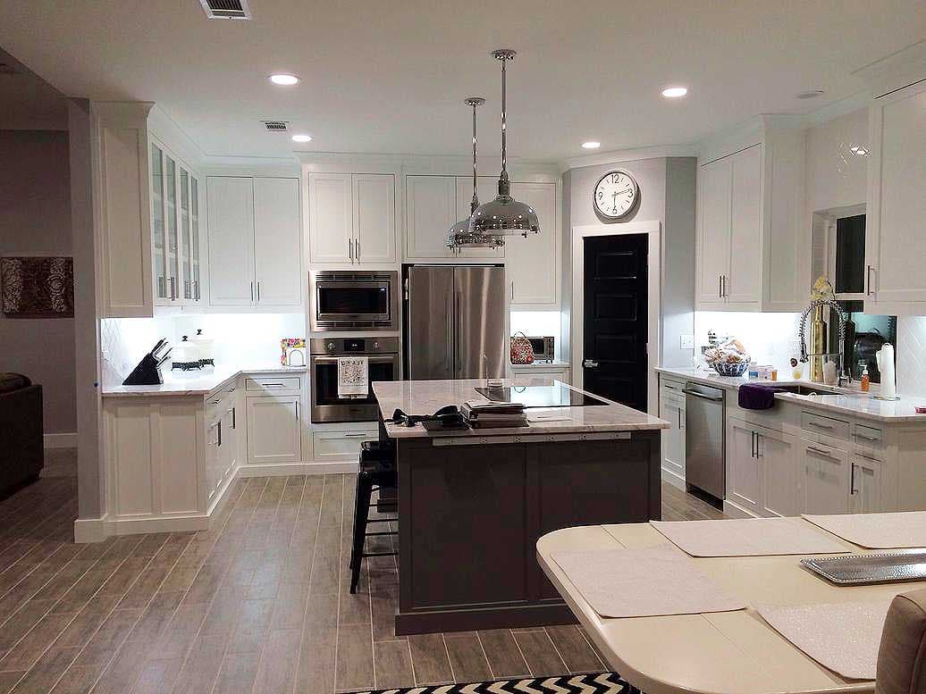 Kitchen with white cabinetry, stainless steel appliances, large island with cooktop, and wood-look tile flooring.