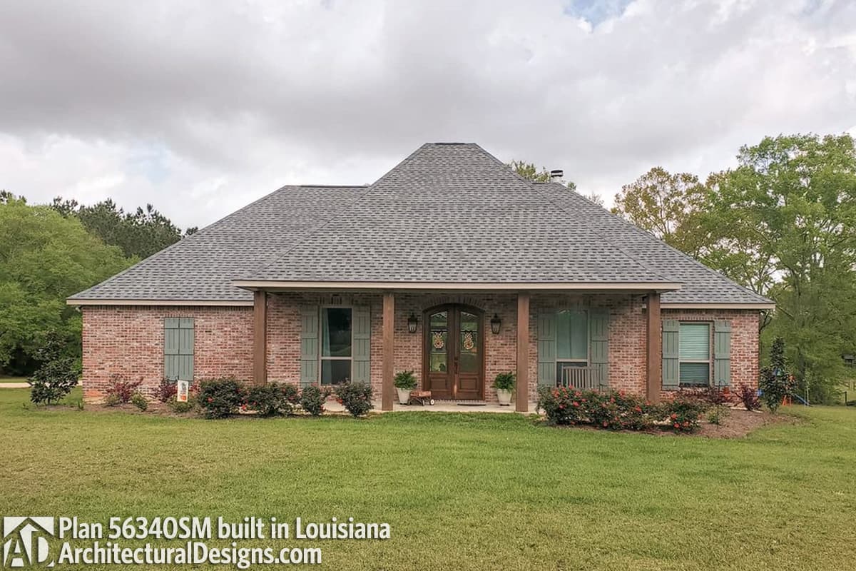 House plan exterior: One-story brick home with a prominent gable roof, covered front porch, double front doors, and green shutters.