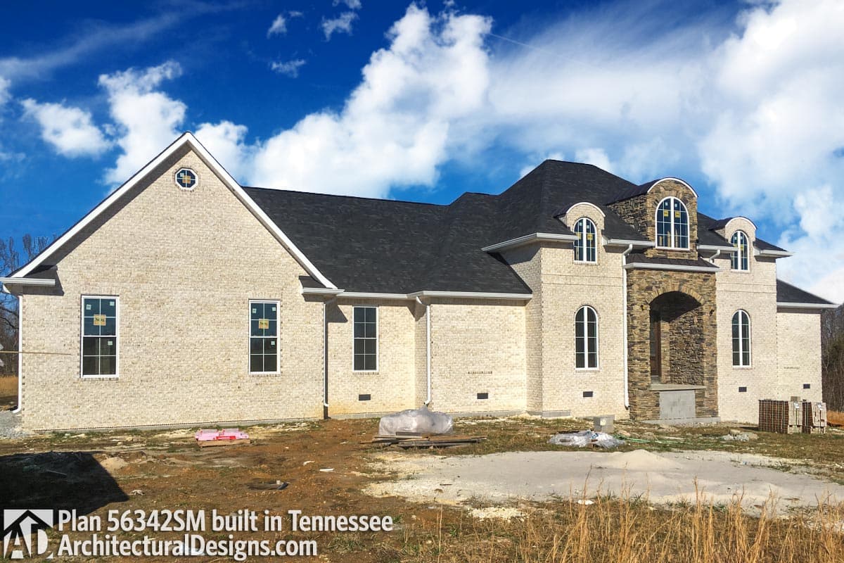 House plan exterior with light brick facade, dark roof, arched stone entryway, and gabled front with circular window.