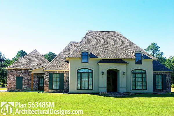 House plan exterior with brick accents, arched windows, dormers, and a prominent arched entry with decorative lighting.