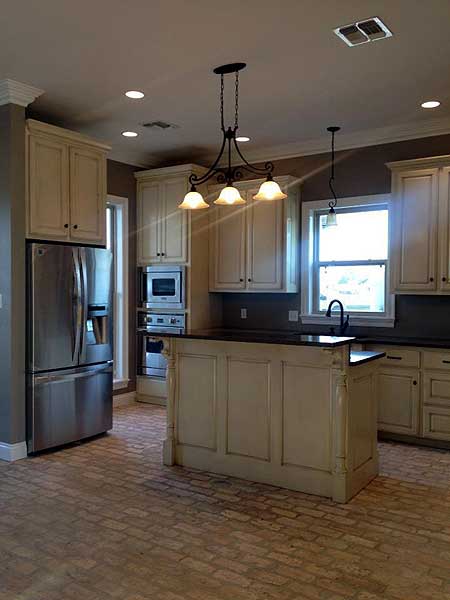 Kitchen interior with stainless steel refrigerator, island with pendant lights, and cream-colored cabinetry.