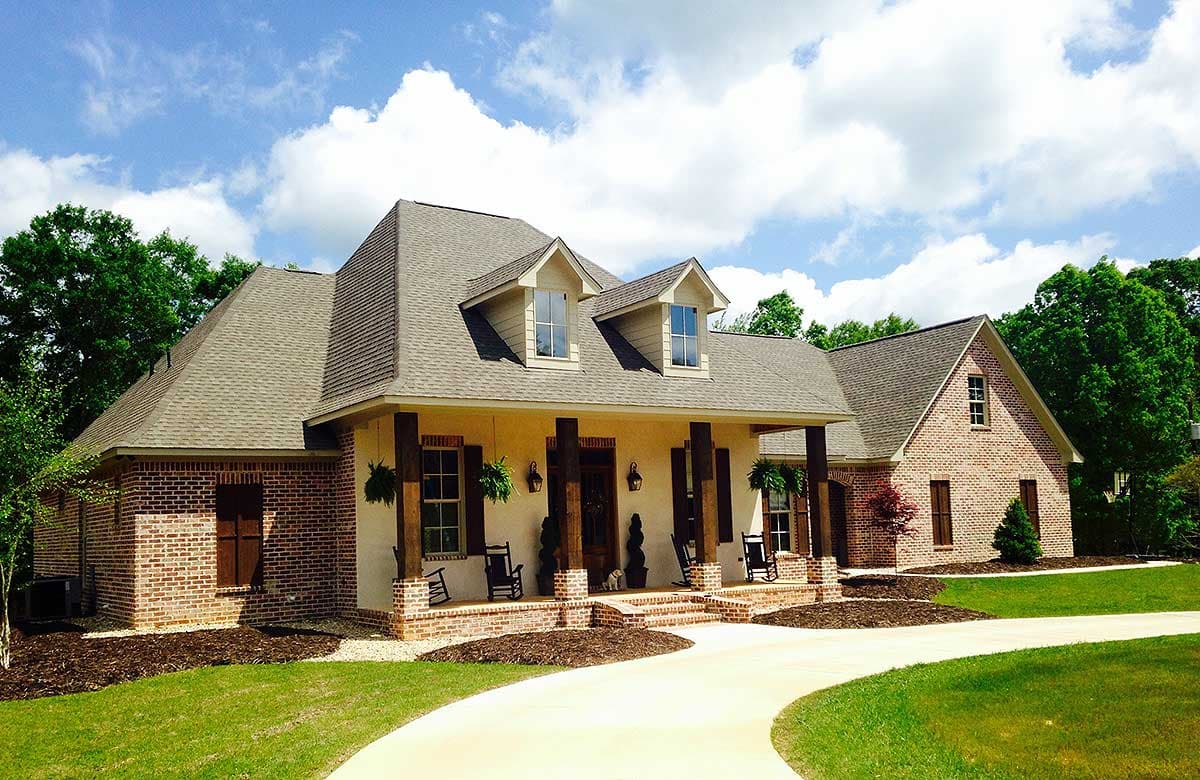 House plan exterior featuring a wide, covered front porch with brick pillars, dormer windows, and a brick and stucco facade.