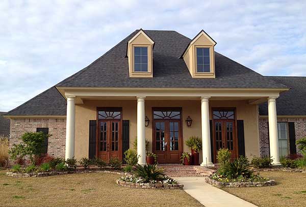 House plan exterior with a prominent covered porch supported by columns, dual dormer windows, and brick and stucco finishes.