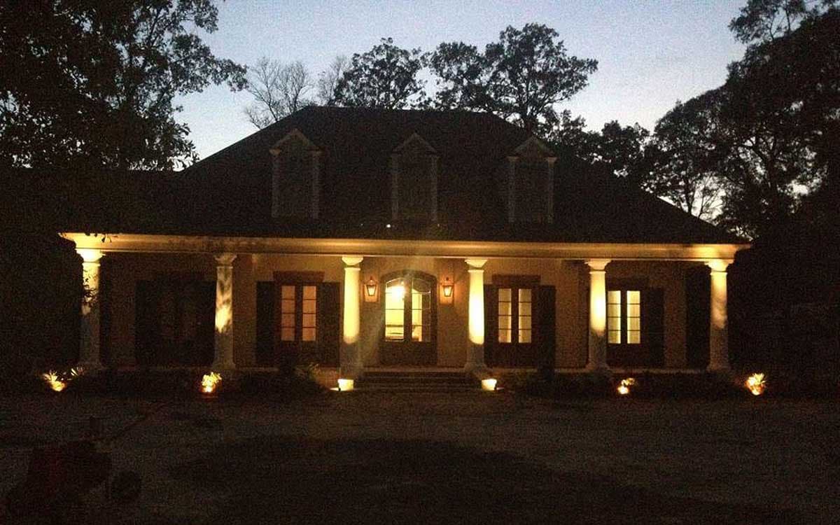 House plan exterior: one-story home with a full-width covered porch supported by Doric columns, dormer windows, and shutters.