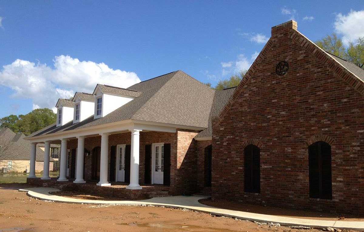 House plan exterior: brick construction, expansive covered porch with columns, multiple dormer windows, and gabled rooflines.