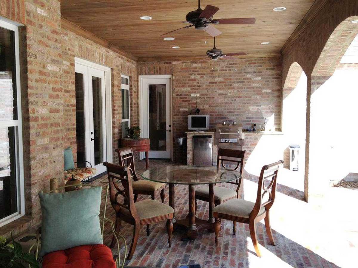 Covered outdoor patio with brick walls, wood ceiling, ceiling fans, outdoor kitchen, and dining set.