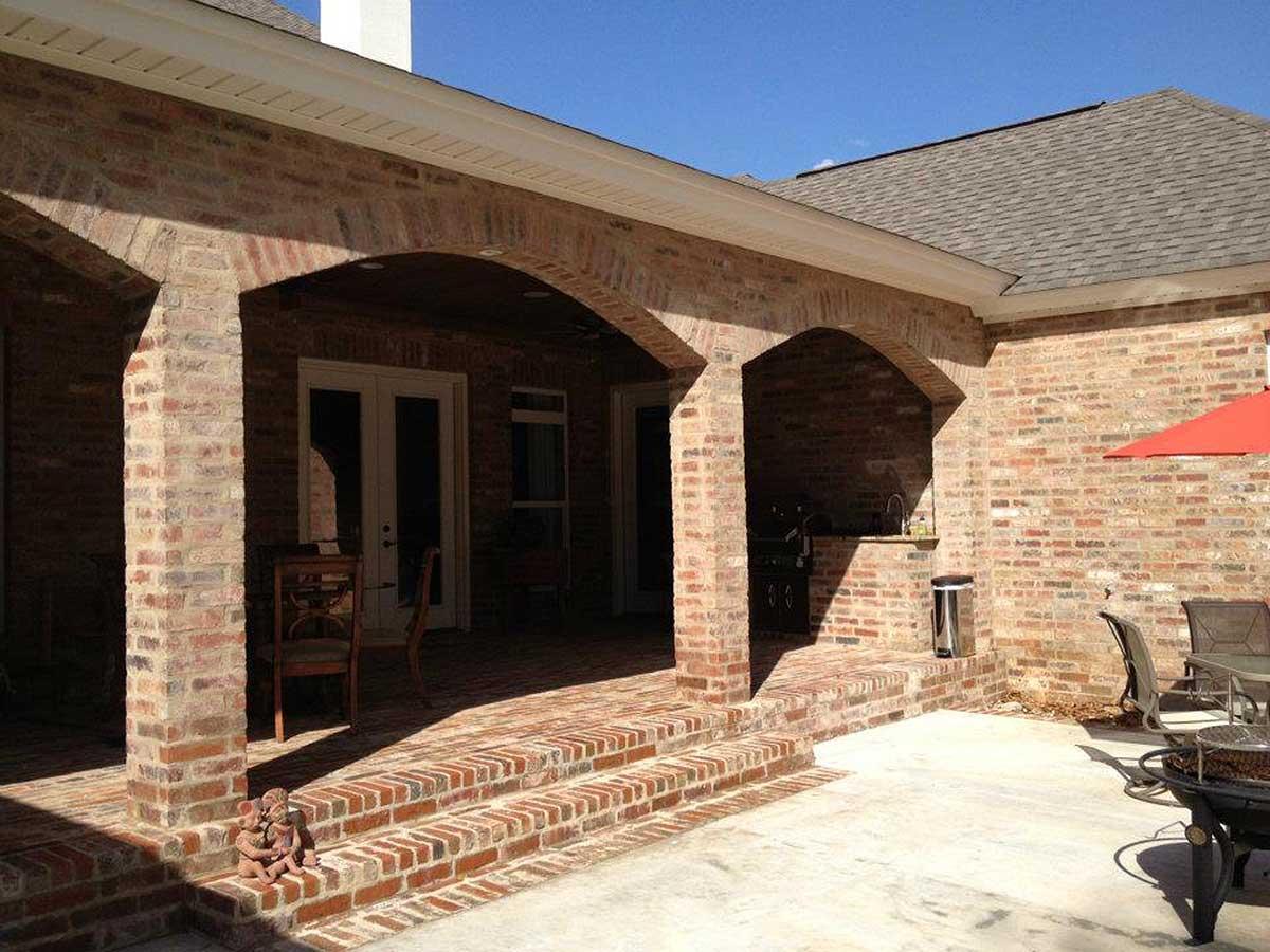 Exterior house plan with brick exterior, covered porch with arches, and outdoor kitchen.