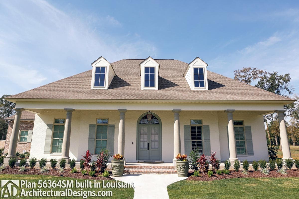 House plan exterior: One-story home with hip roof, three dormer windows, central arched entryway, and a covered porch supported by columns.
