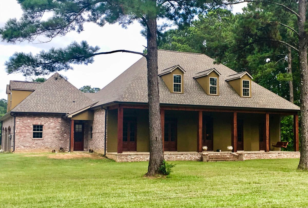 House plan exterior with brick accents, a wide covered porch with timber supports, and three dormer windows.