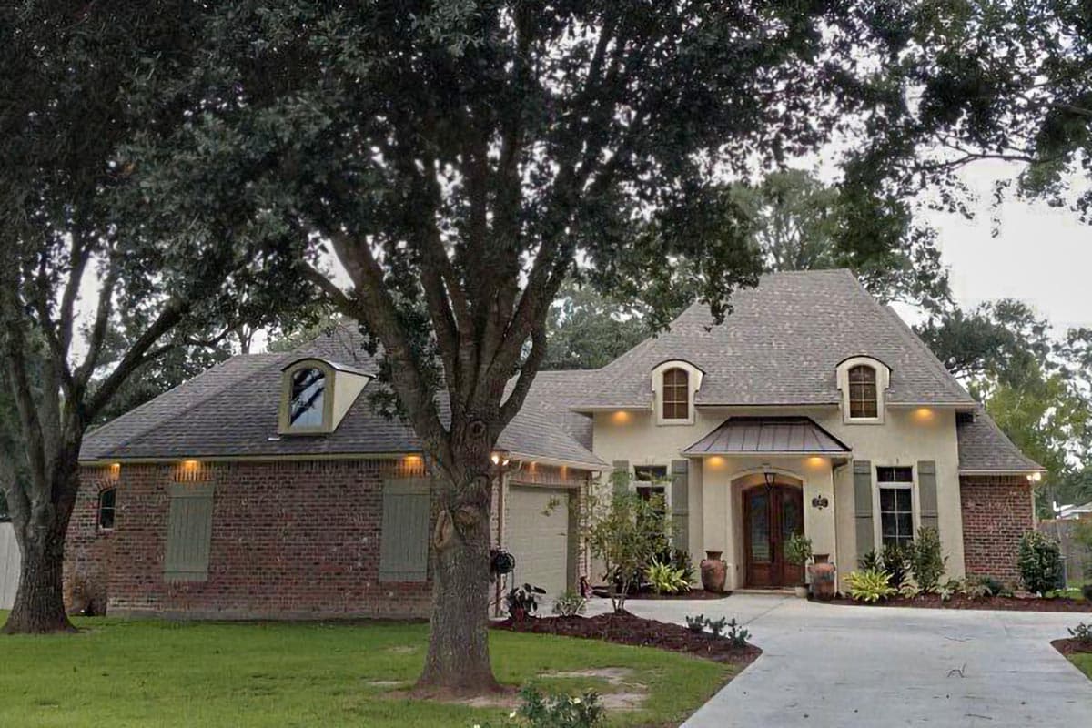 House plan exterior featuring a mix of brick and stucco, hip rooflines, arched dormers, and a prominent front entrance.