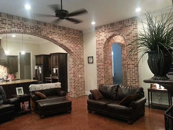 Interior view showing a living area with brick archways connecting to a kitchen, dark leather sofas, and a ceiling fan.