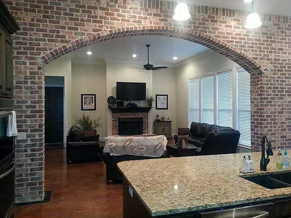 Interior view of a living room with a brick archway, fireplace, sectional sofa, and large windows.