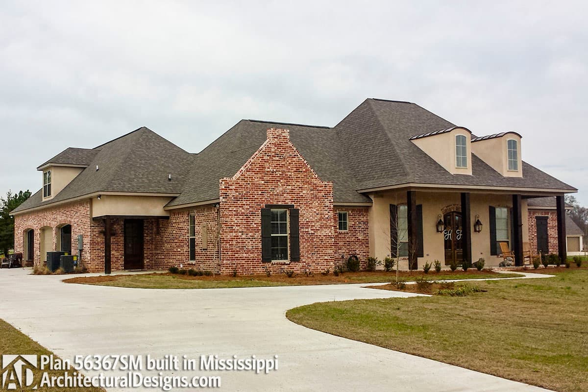 House plan exterior: brick and stucco, complex rooflines, arched dormers, covered porch with columns, and a three-car garage.