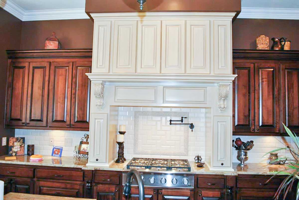 Kitchen range with ornate hood, white subway tile backsplash with decorative insert, and dark wood cabinetry.