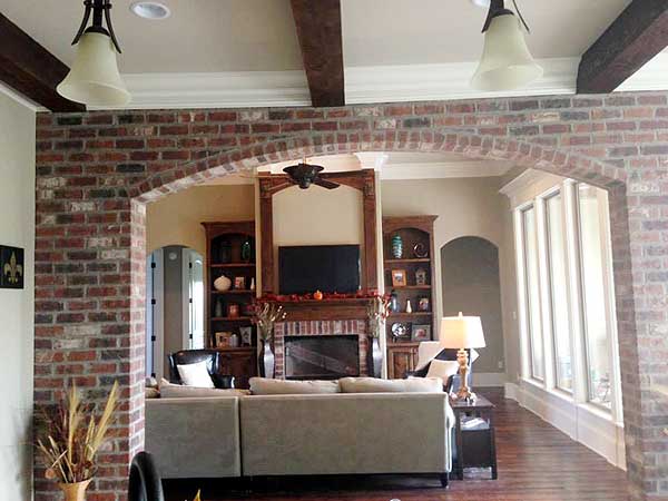 Interior view of living room with fireplace, built-in bookshelves, exposed beams, and large windows.