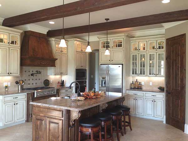 Kitchen with wood beam ceiling, large wooden range hood, granite island with seating, and cream cabinets.