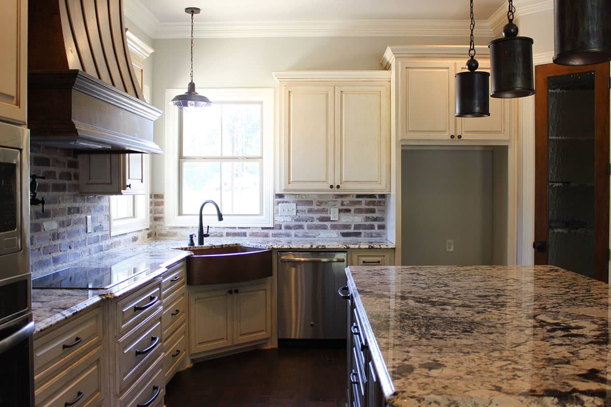 Kitchen with a copper farmhouse sink, granite countertops, brick backsplash, stainless steel dishwasher, and a large island.
