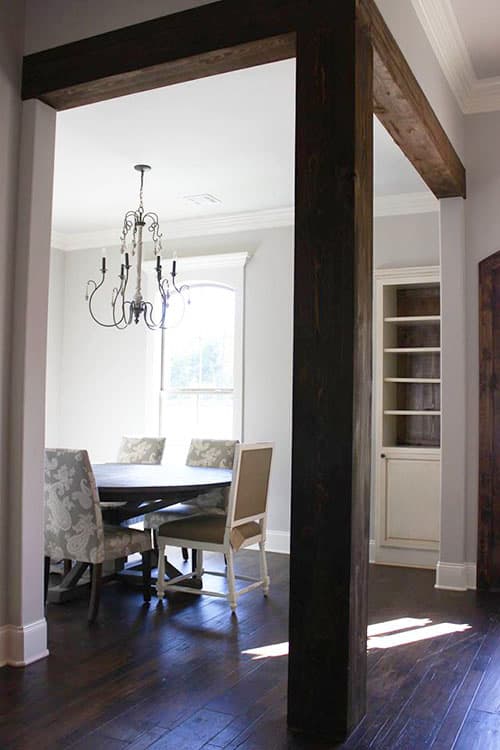 Dining room with dark wood beams, chandelier, built-in shelving, and round table with chairs.