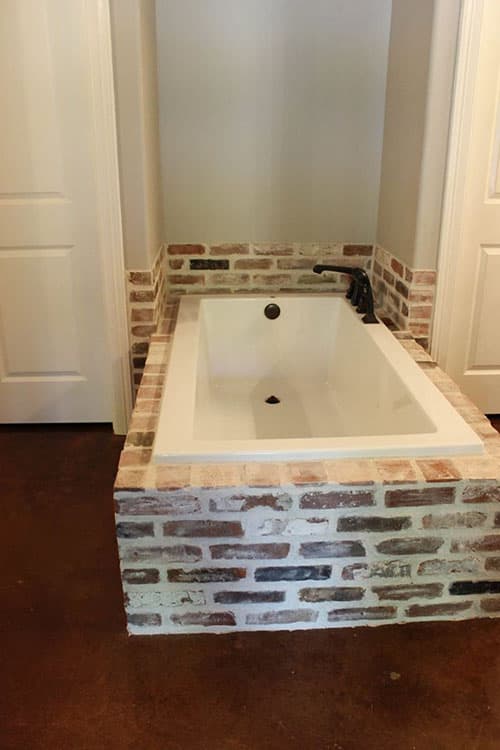 Bathroom with freestanding tub on a raised brick hearth, dark floor, and two white doors.