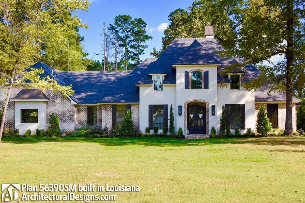 House plan exterior: white stucco and brick, hip roof, arched entry, multiple gables, large windows, dark shutters.