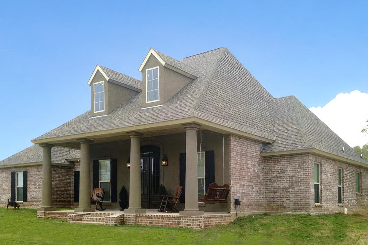 House plan exterior: two-story brick home with a wraparound porch, column supports, and dormer windows on a steep roof.