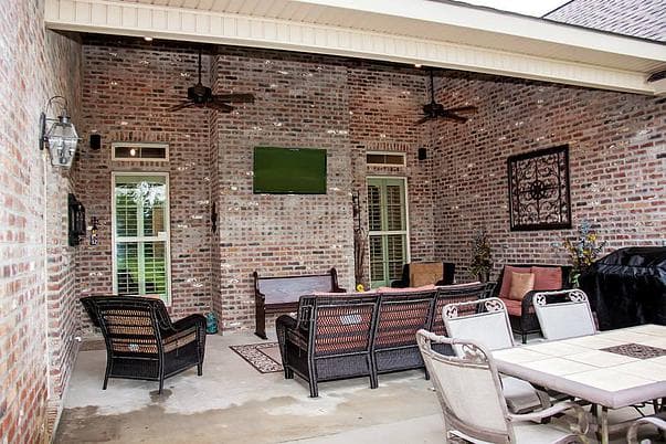 Covered patio with brick walls, ceiling fans, seating, dining table, and outdoor television.