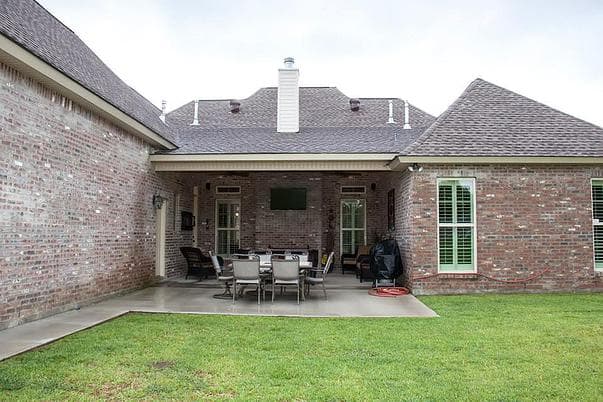 House plan exterior with brick walls, covered patio, outdoor dining set, fireplace, and television.