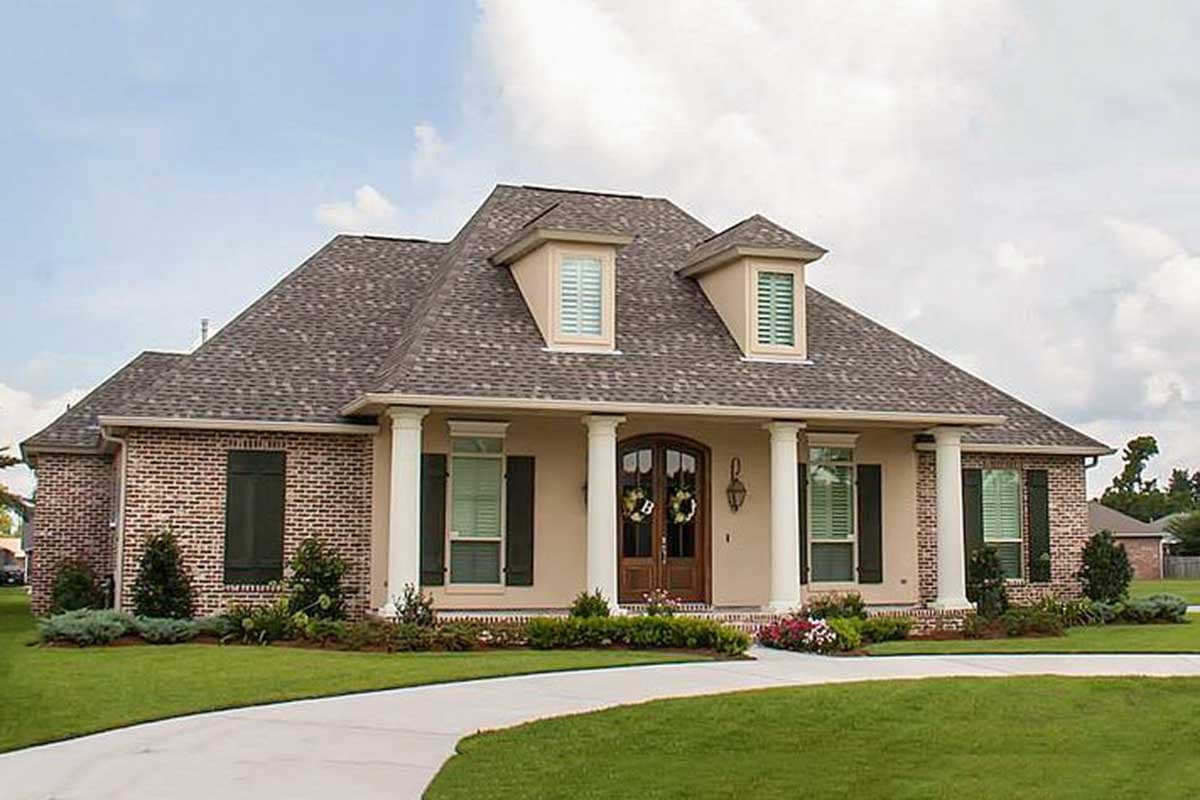 House plan exterior: Brick and stucco one-story home with a prominent portico, dormer windows, and a sweeping driveway.