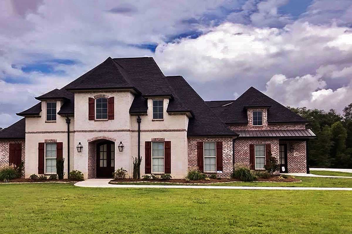 House plan exterior of two-story home with arched entryway, brick accents, dormers, and dark hip roof.