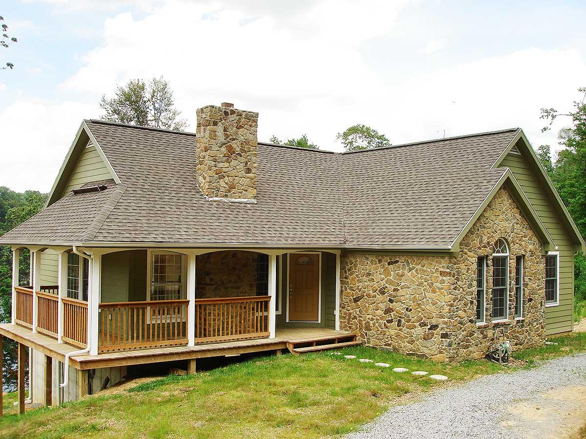 House plan exterior featuring stone facade, prominent chimney, wraparound porch, and multi-level rooflines.