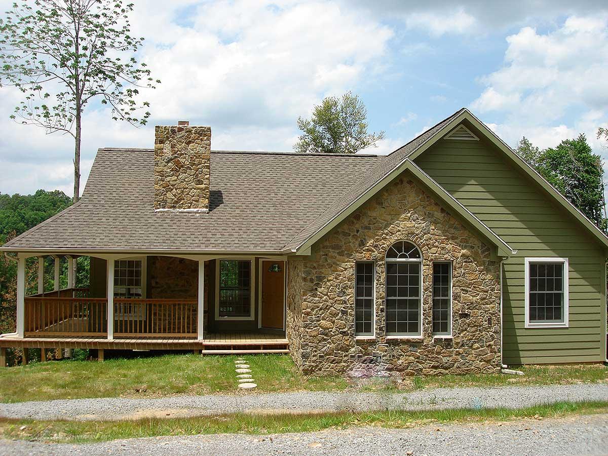 House plan exterior: Stone facade with arched window, porch, gabled roof with green siding and stone chimney.