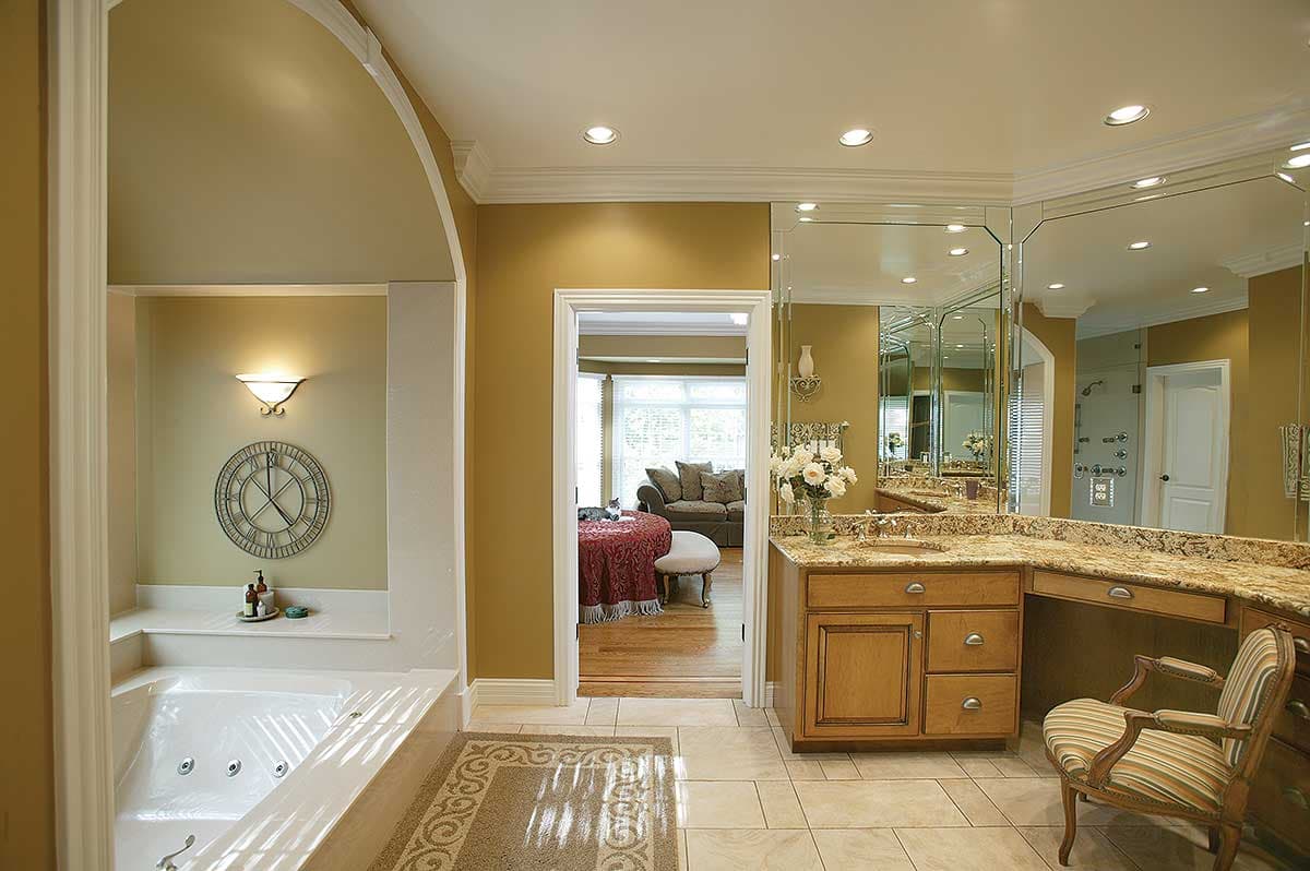 Bathroom with large jacuzzi tub, vanity with granite countertop, multi-panel mirror, and arched doorway to living area.