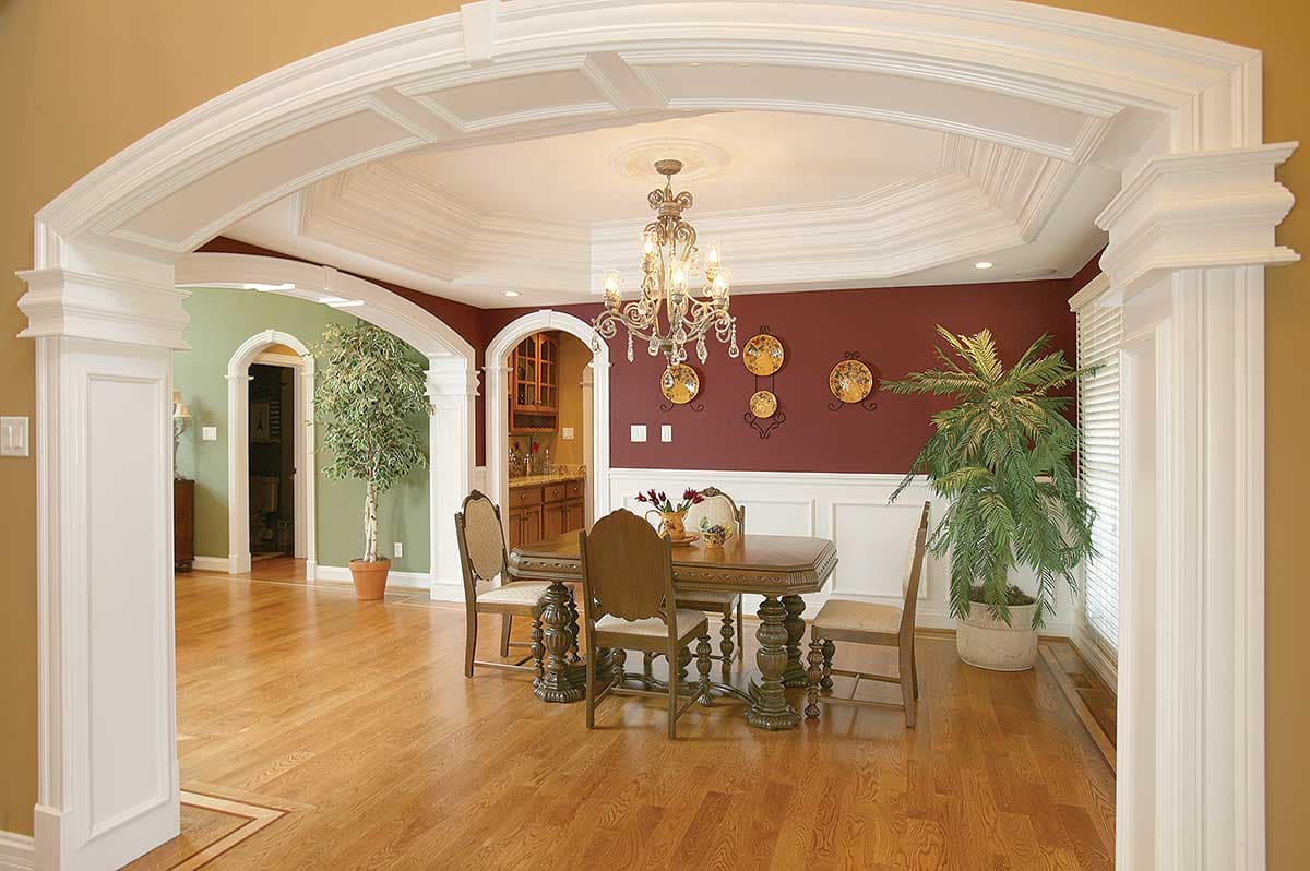 Interior view of dining room with coffered ceiling, chandelier, arched doorways, and wainscoting.