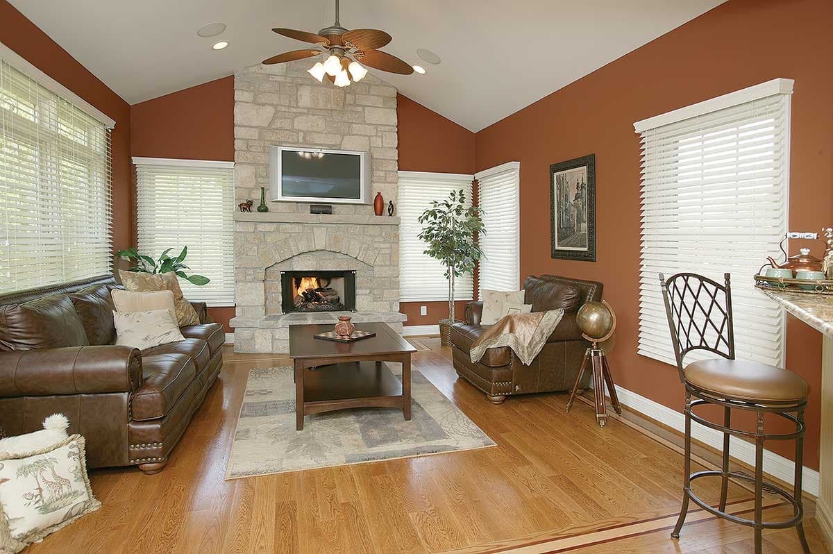 Great room with vaulted ceiling, stone fireplace with TV, leather sofa, armchair, coffee table, and bar stool.