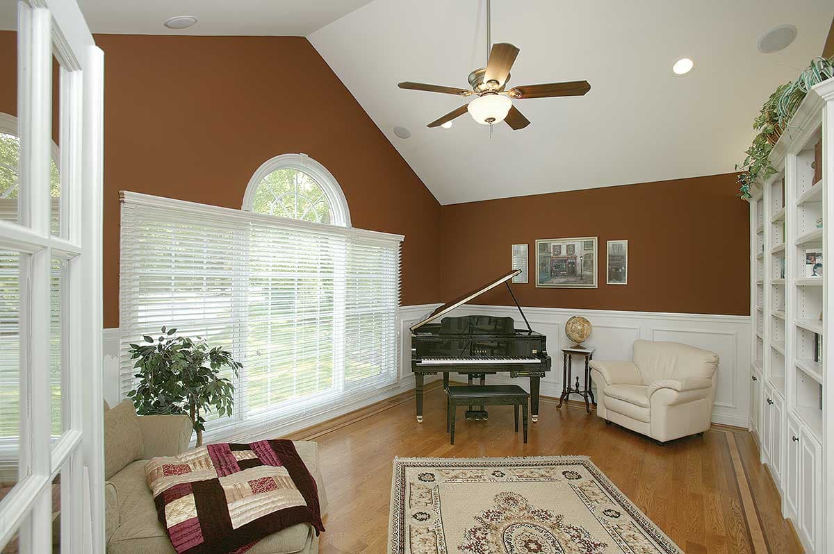 Interior view of a living room with vaulted ceiling, grand piano, large windows, and built-in bookshelves.