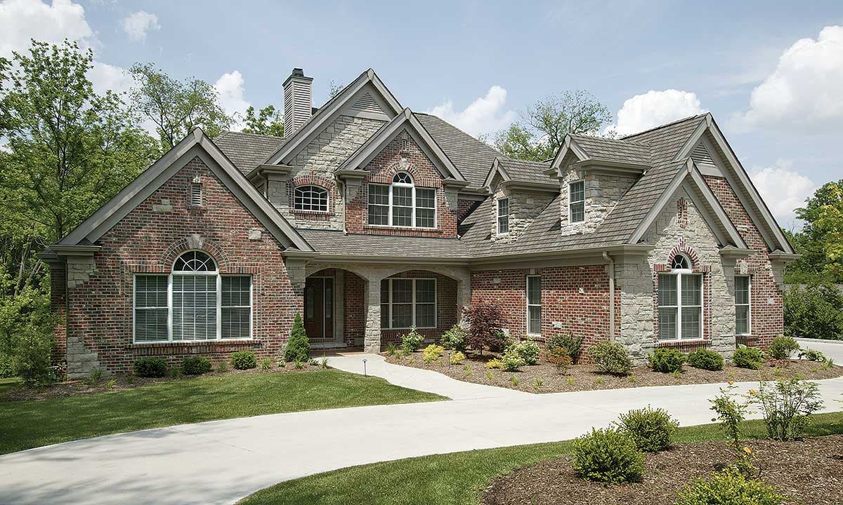 House plan exterior with brick and stone facade, arched windows, gables, and covered entryway.