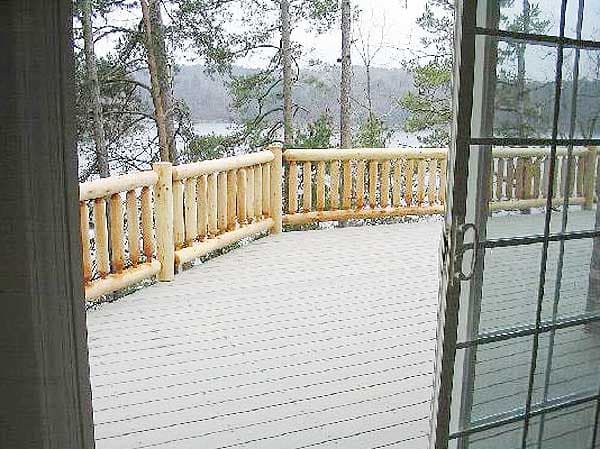 Deck with natural log railing and grey decking overlooking a wooded lake view. Sliding glass door visible.