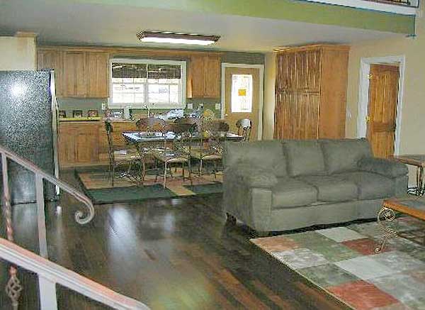 Open concept living area with kitchen, dining table with chairs, and sofa. Wood cabinetry and flooring visible.