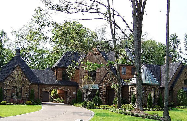House plan exterior showing a multi-story stone and brick home with arched porte-cochère, conical turrets, and multiple gables.