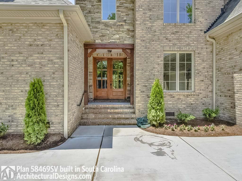 House plan exterior with stone accents, wooden double doors, and multi-pane windows.
