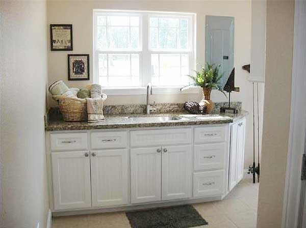 Laundry room counter with granite top, white cabinets, sink, and double-hung window.