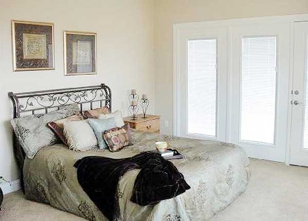 Bedroom with wrought iron headboard, decorative pillows, and two glass doors with blinds.