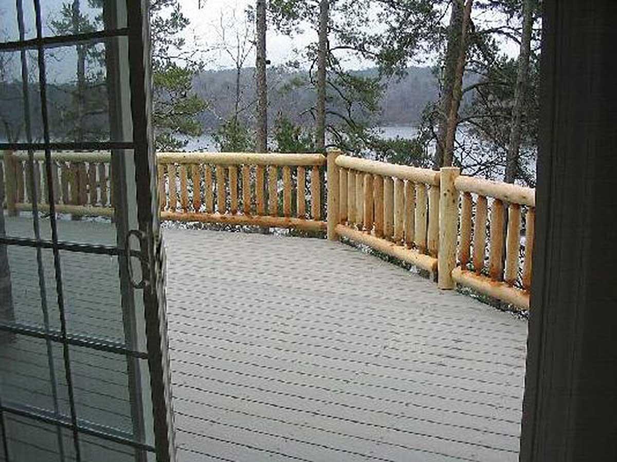 House plan exterior featuring a deck with a log railing, overlooking a wooded area and water.