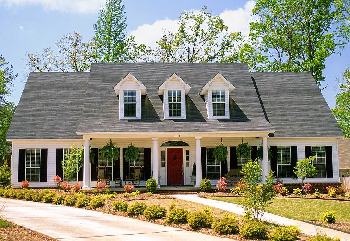 House plan exterior: Traditional style, one-story with a covered front porch, central red door, three dormers, and shutters.