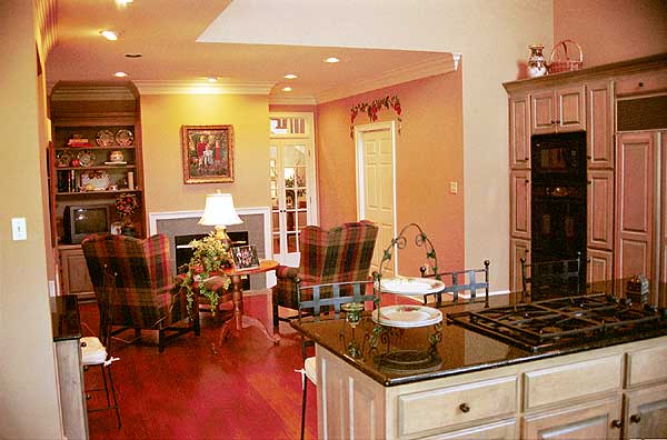 Open living area with fireplace, built-in shelving, kitchen island with gas range, and plaid upholstered chairs.